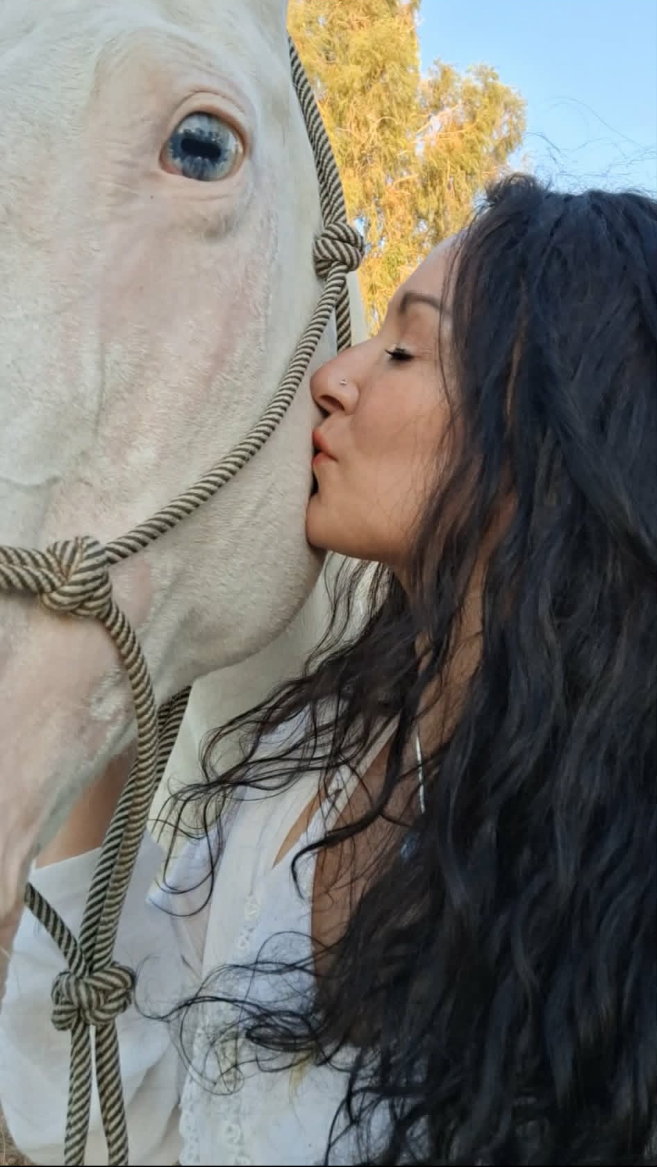Claudia Rubio kissing a white horse with blue eyes
